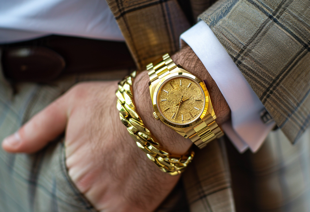 man’s wrist wearing a classy gold watch paired with a flashy gold cuban-link bracelet