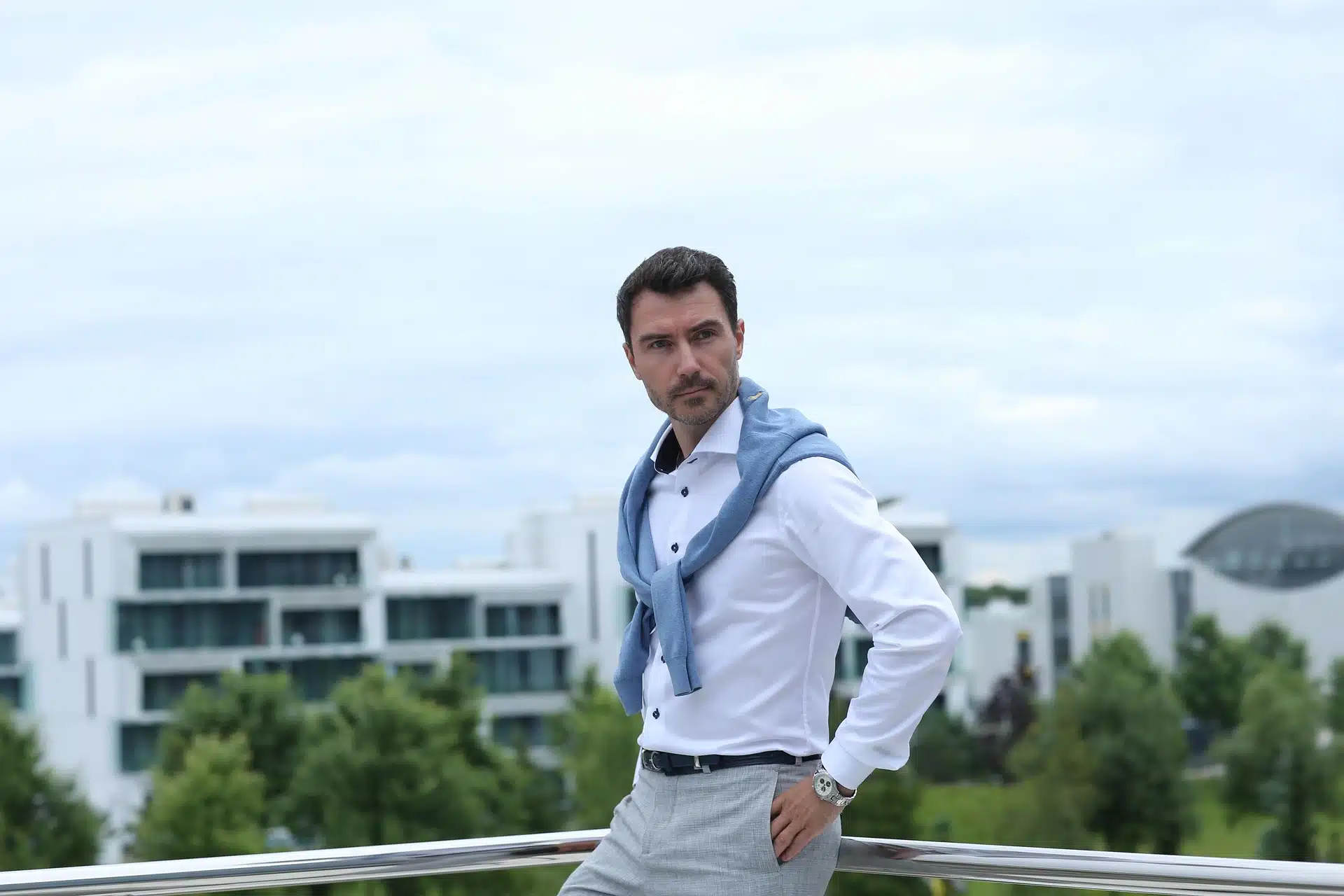 A man standing on the roof of a building wearing a white dress shirt with light grey dress pants.
