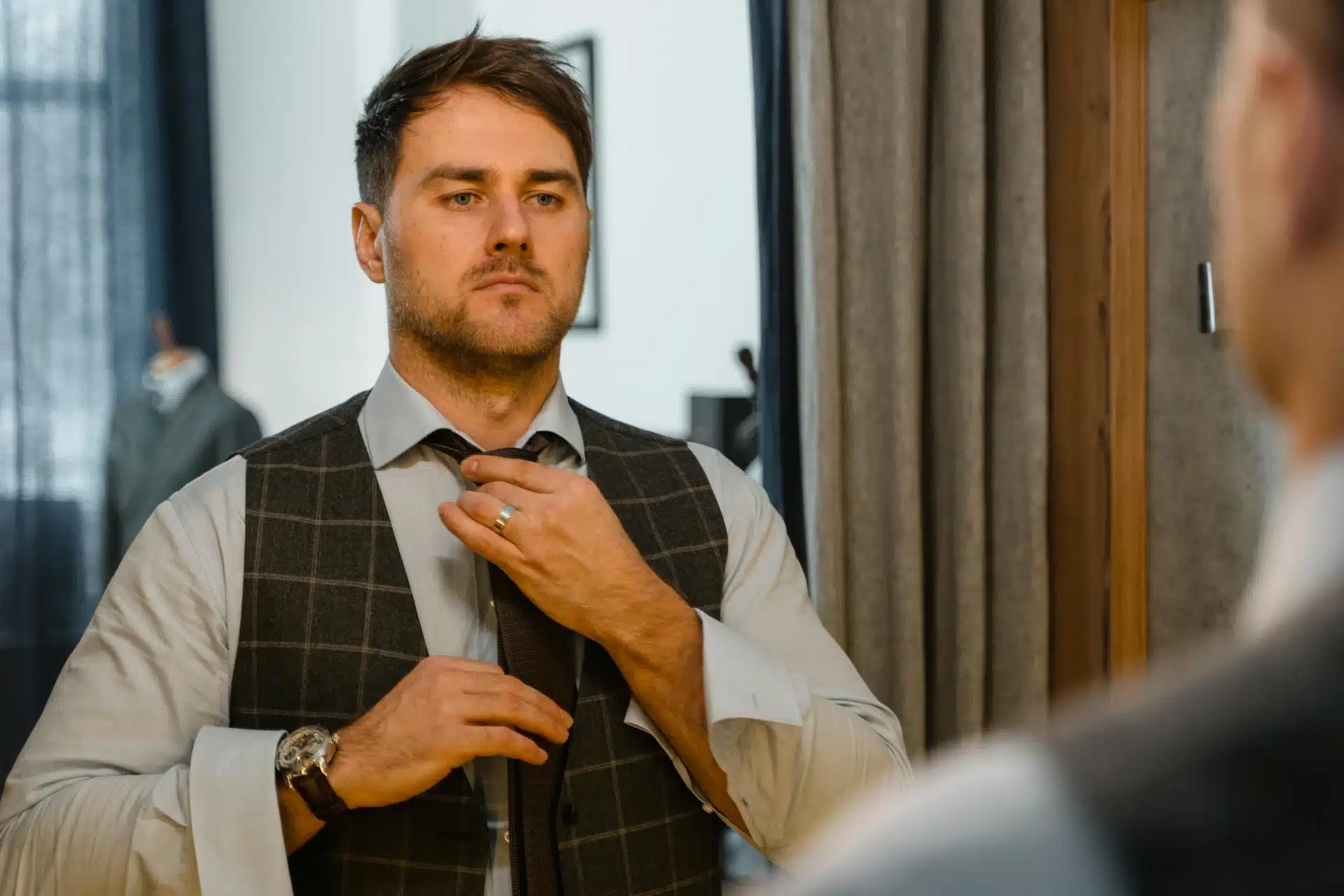 A man standing in front of a mirror adjusting his necktie.