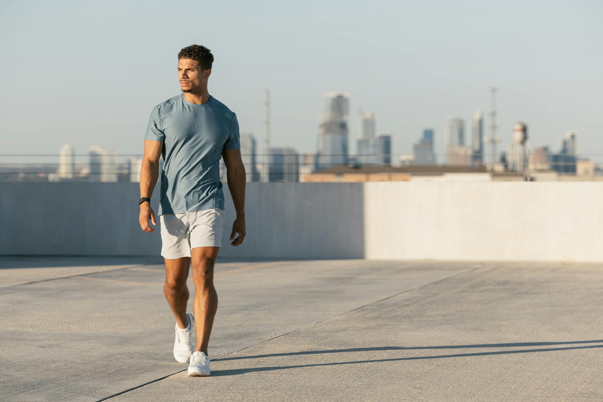 A muscular man on the roof of a building wearing a fitted t-shirt with fitted shorts.