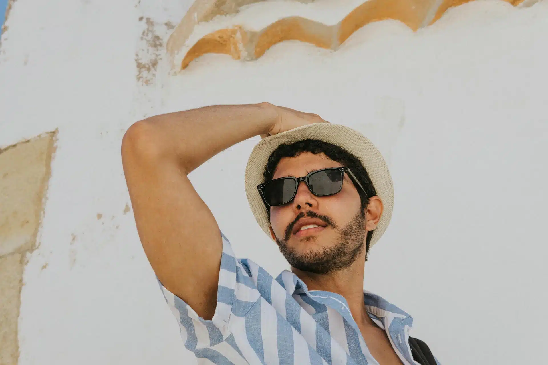Man in Blue and White Stripe Polo Shirt Wearing Black Sunglasses and Brown Hat.