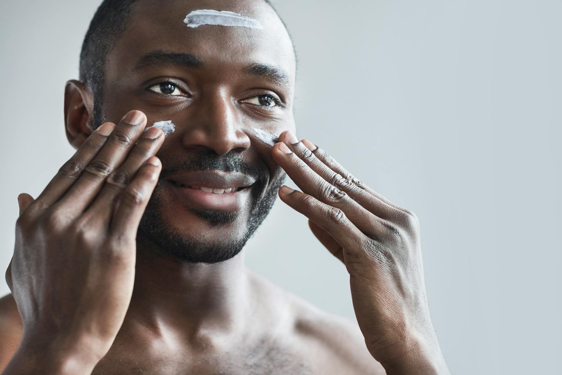 A man of African descendent applying cream on his face.