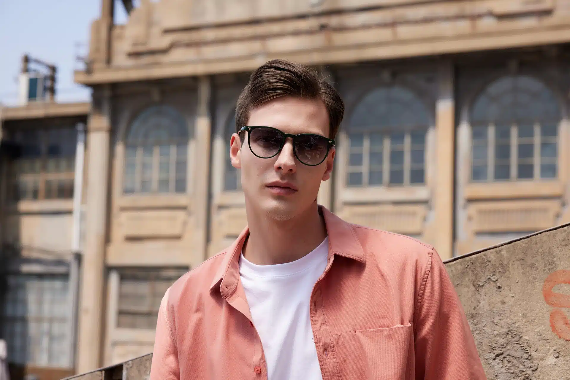 A young man in sunglasses wearing a salmon shirt over a white t-shirt.