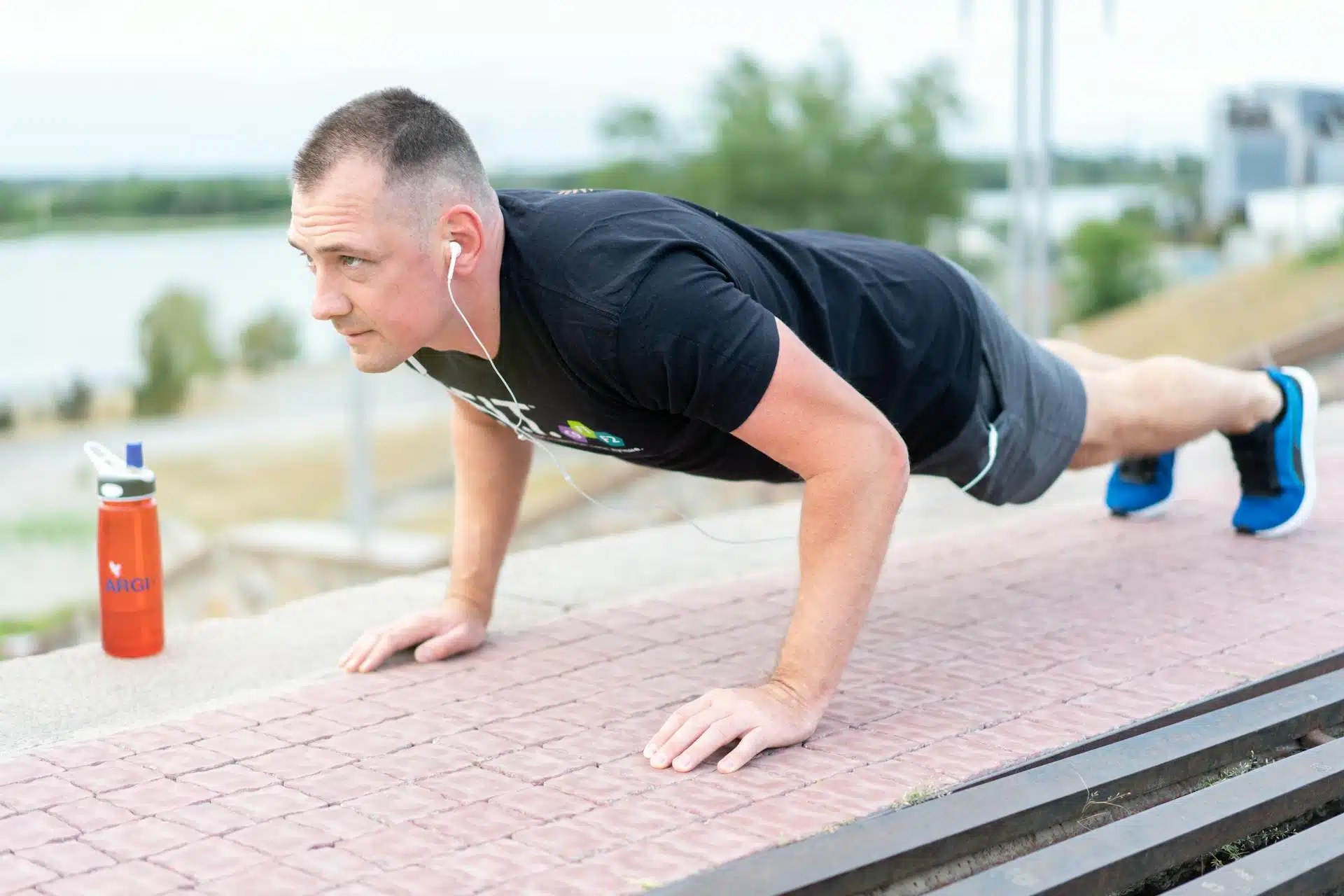 Man doing pushups outdoors with wired headphones in his ears.