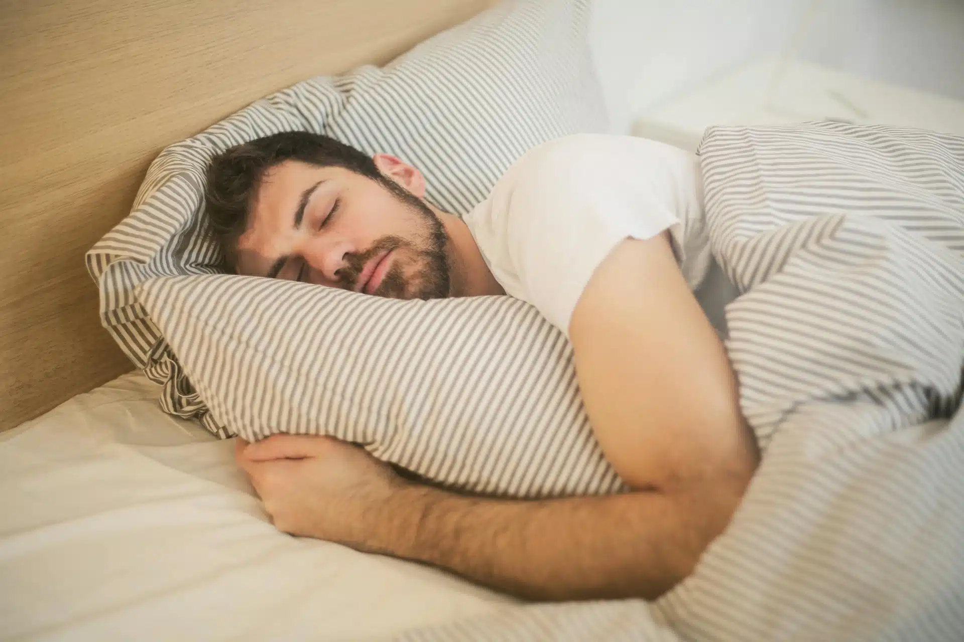 Man sleeping on a striped pillow while hugging another pillow.
