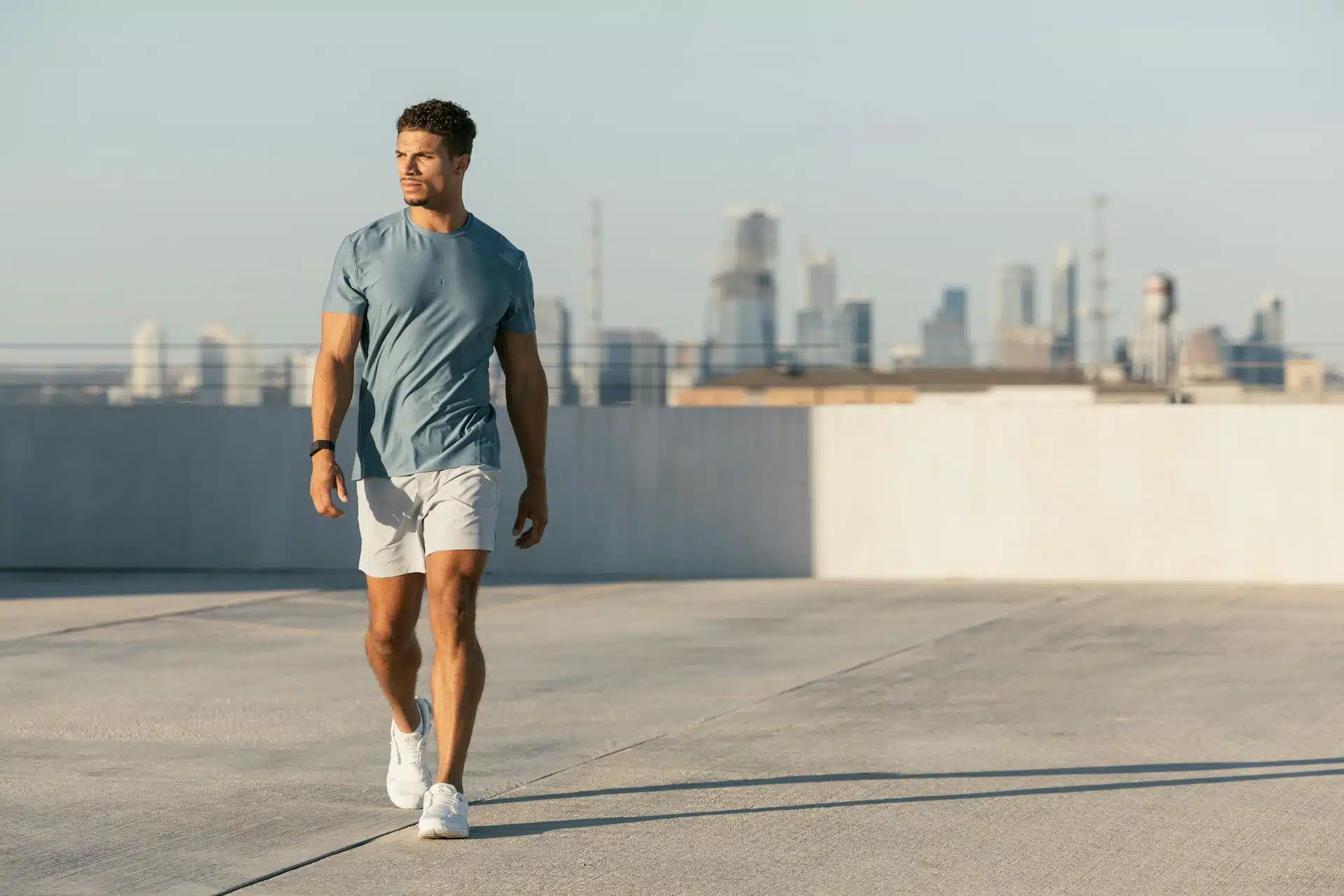 A muscular man on the roof of a building wearing a fitted t-shirt with fitted shorts.
