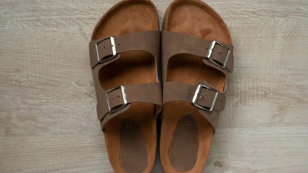 An overhead view of a pair of brown leather sandals placed on a wooden floor.