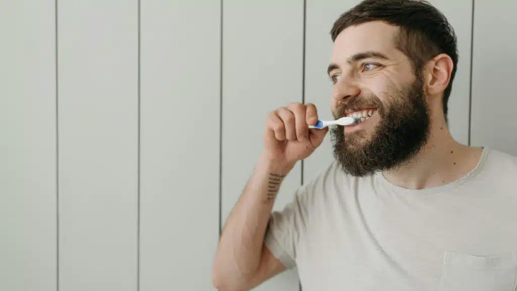 Bearded man in a crew neck t-shirt brushing his teeth.