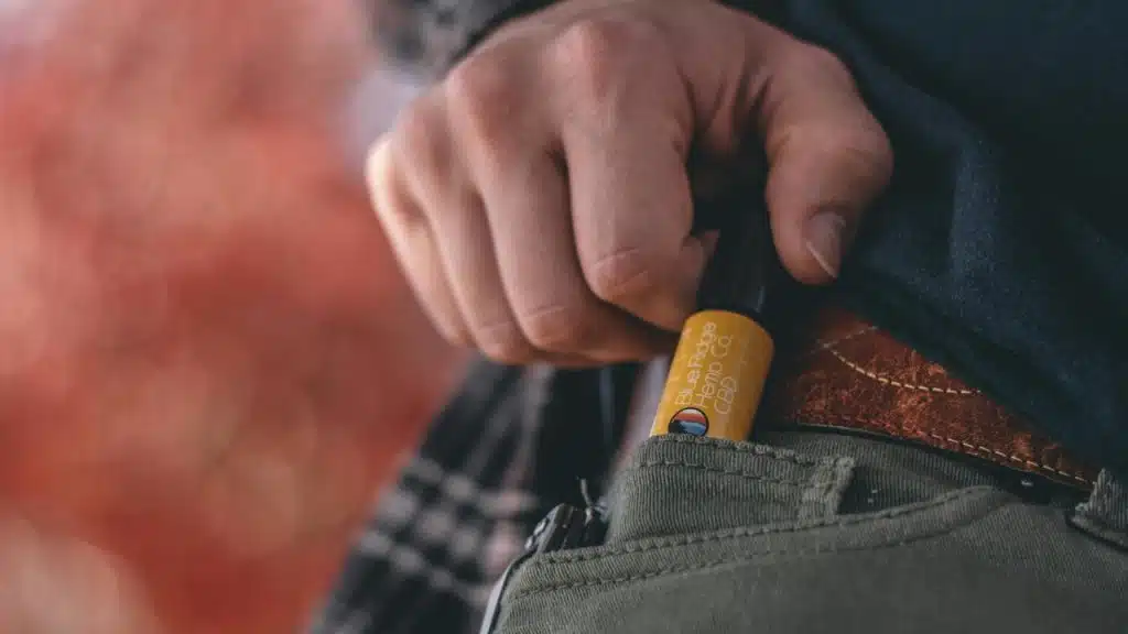 Close-up of a man pulling a small sunscreen container from the coin pocket of his jeans.