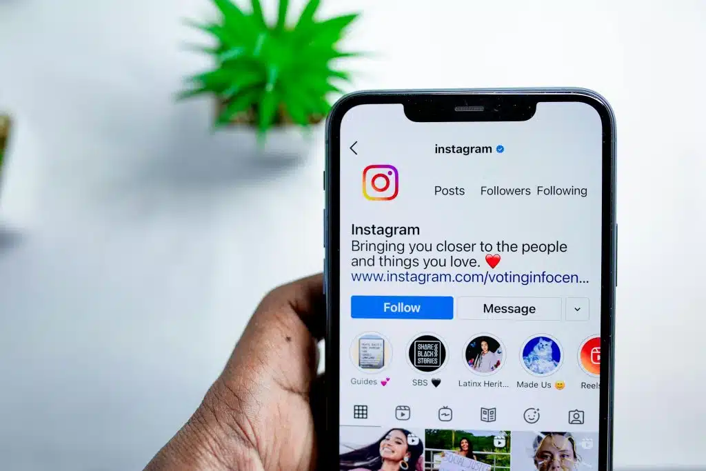 Close-up of a person holding up a smartphone displaying an Instagram account's feed.