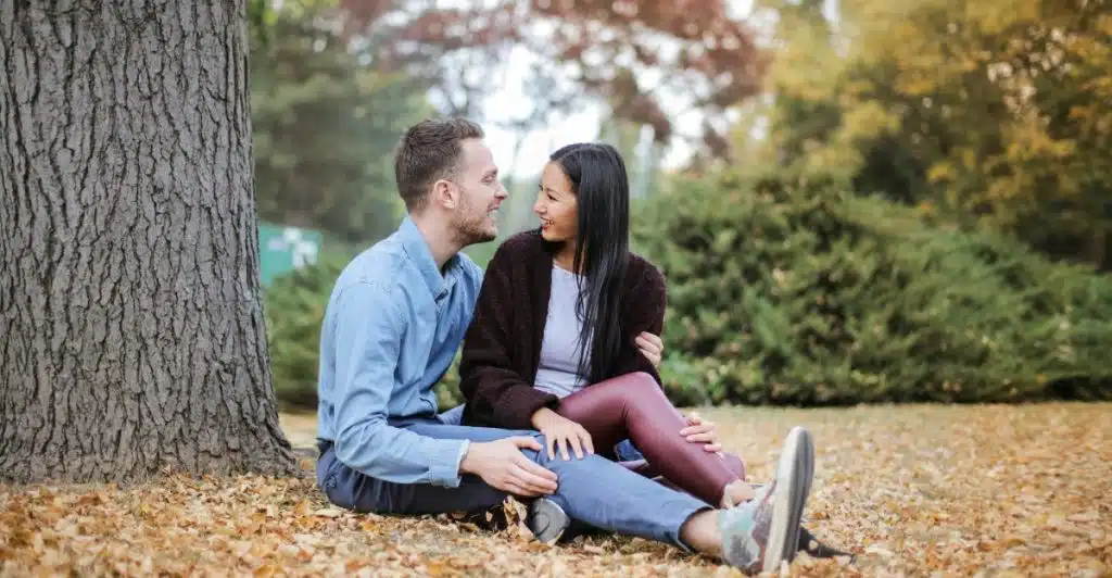 Couple sitting on dried leaves under a tree.