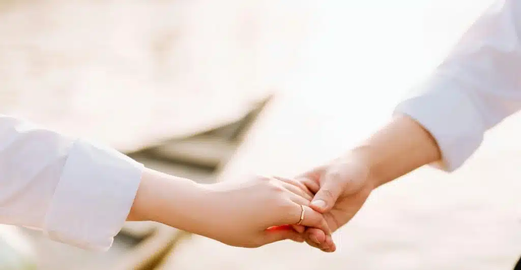 Close-up of a couple holding hands, with a ring in the woman's index finger.