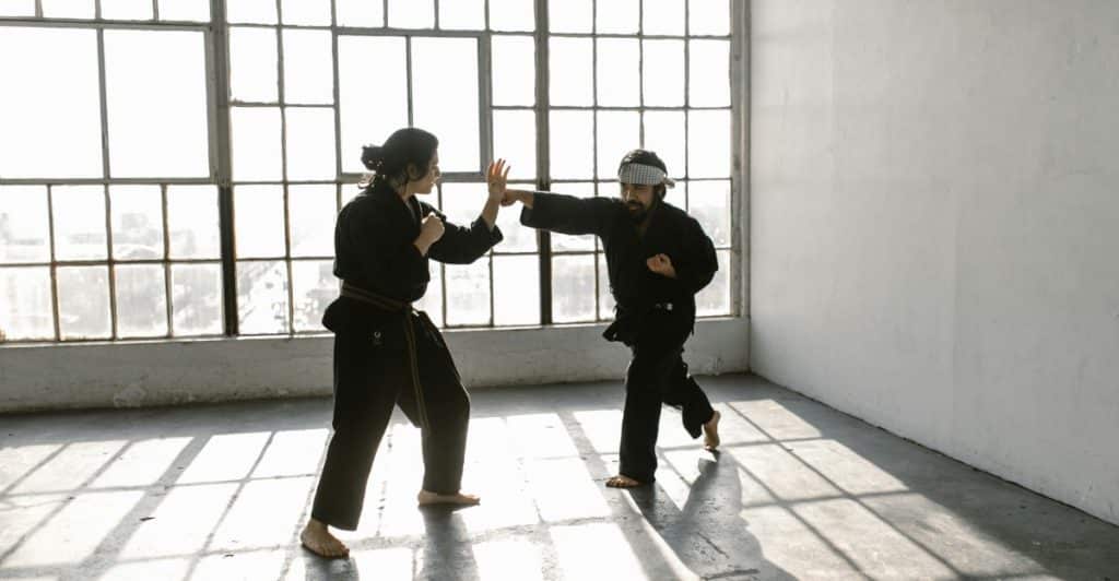 Two persons practicing Karate in an empty room with a big window.