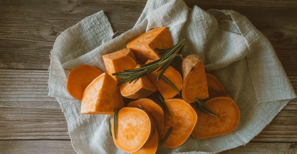 Slices of sweet potatoes on a piece of fabric placed on a wooden surface.