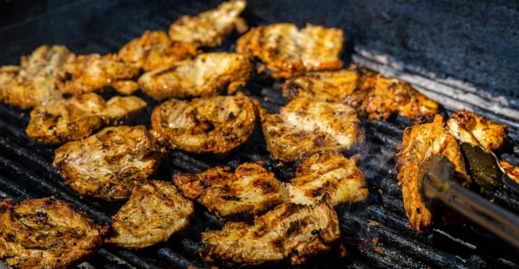 Chicken thighs sizzling on a grill.