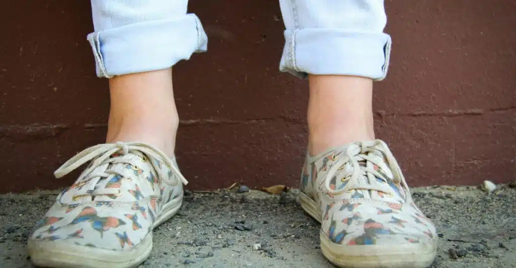 Close-up of legs wearing cuffed light wash jeans and white patterned low-top sneakers.