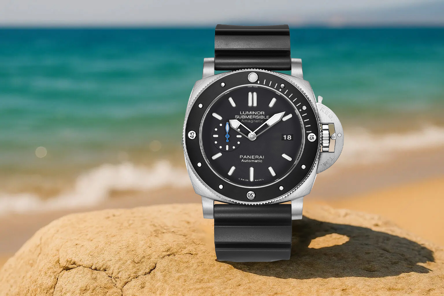 Panerai Luminor Submersible dive watch with a black dial and rubber strap, displayed on a rock with a blurred turquoise ocean background
