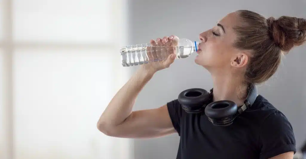 A woman in athletic wear drinking from a plastic water bottle.