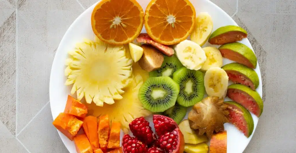 A white plate filled with a variety of sliced fruits, including oranges, kiwi, pineapple, and pomegranate.