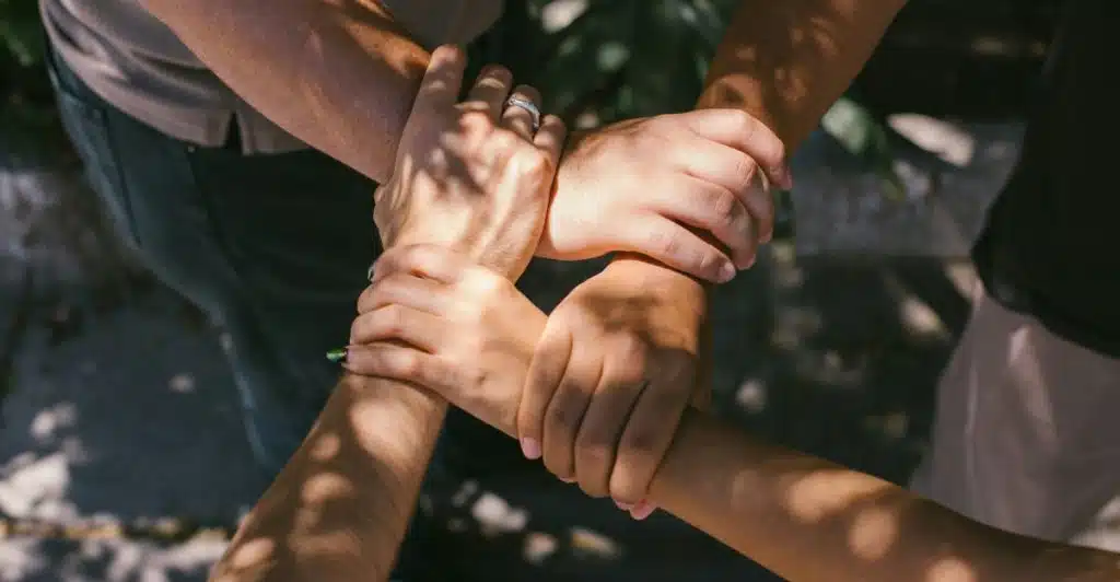 A close-up shot of four hands of different skin tones clasped together in a circle.