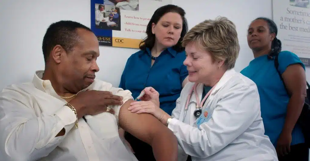 A person receiving a shot in the arm from a healthcare provider in a medical setting.