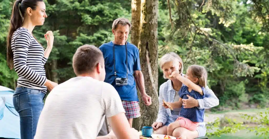 A multi-generational family enjoying a picnic and spending time together in a wooded area.