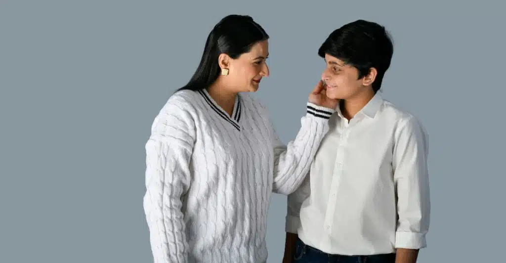  A mother placing her hand on the son's cheek leaning in to talk closely with him, with a neutral background.