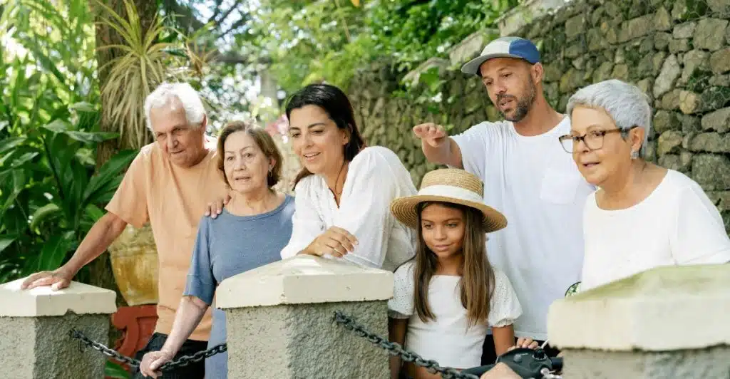 An extended family group standing together outdoors near a stone wall and greenery.