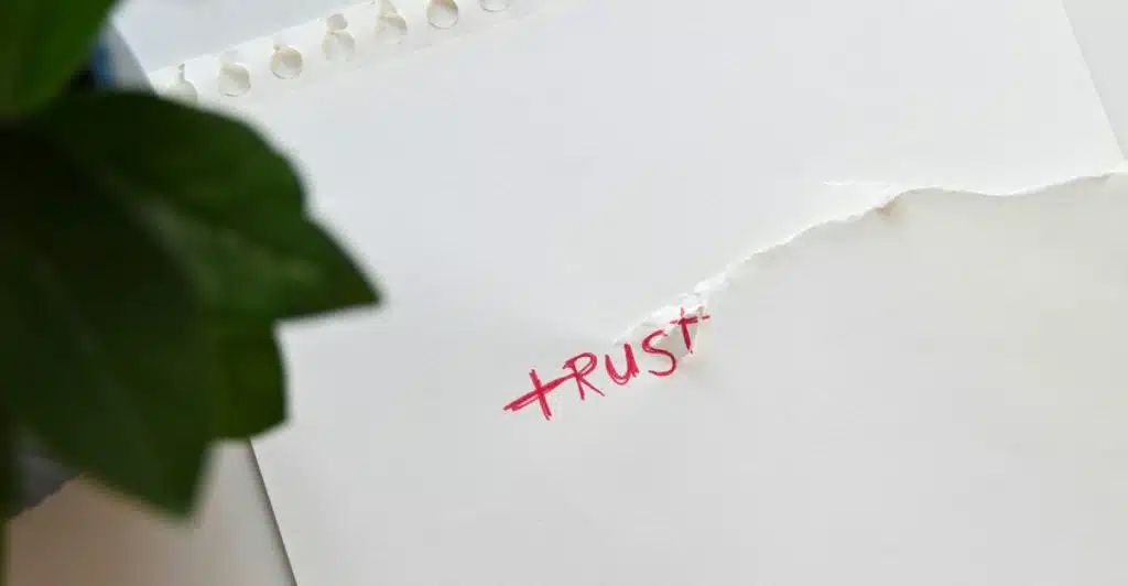 A close-up of a torn piece of paper with the word "trust" written on it.
