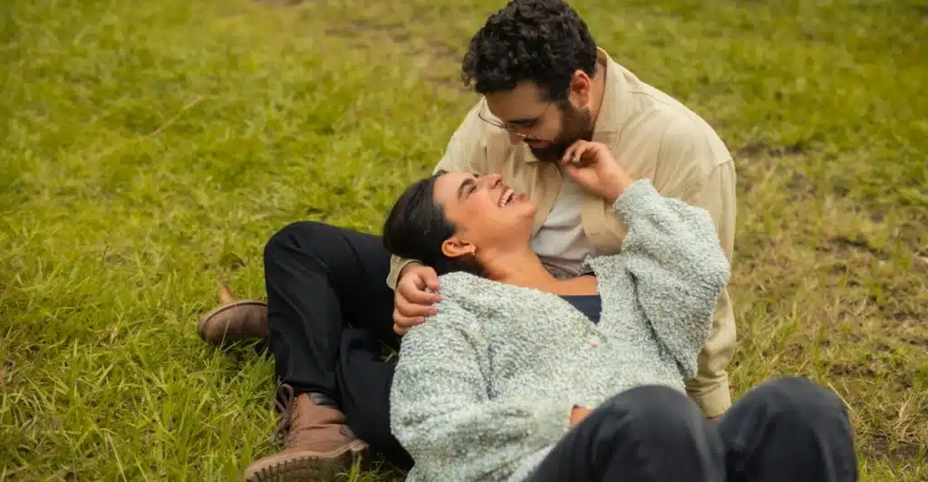 A man and a woman laughing together while lying on the grass.