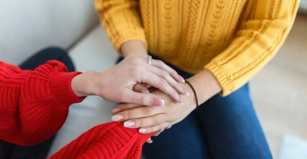 Two people in sweaters holding hands while sitting on a couch.
