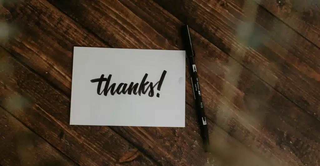 A card with the word "thanks!" written on it and a black pen lying on a wooden surface.