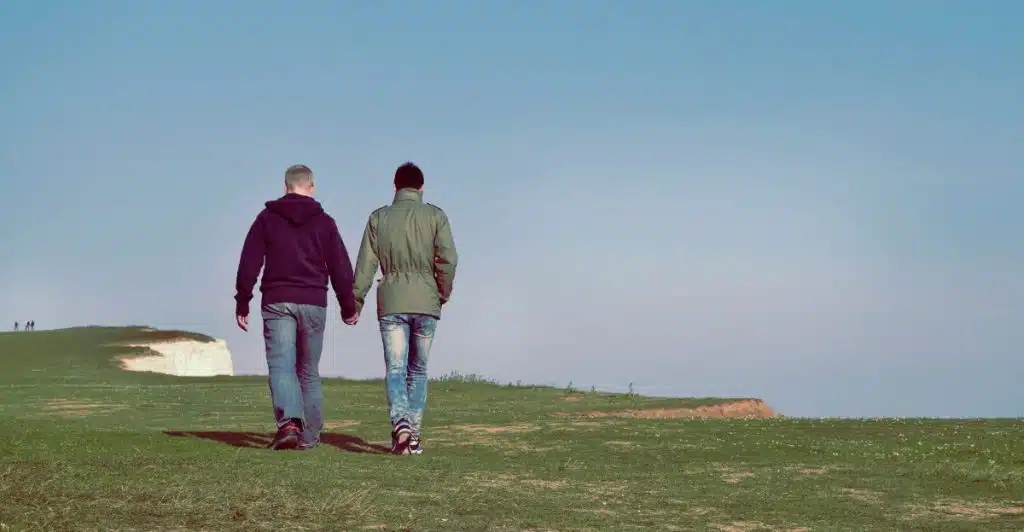 A couple is walking hand in hand on a grassy path.