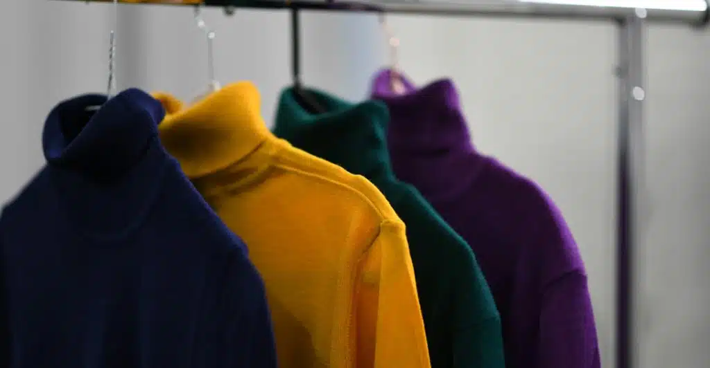 A close-up shot of several colorful turtleneck sweaters hanging on a clothing rack.