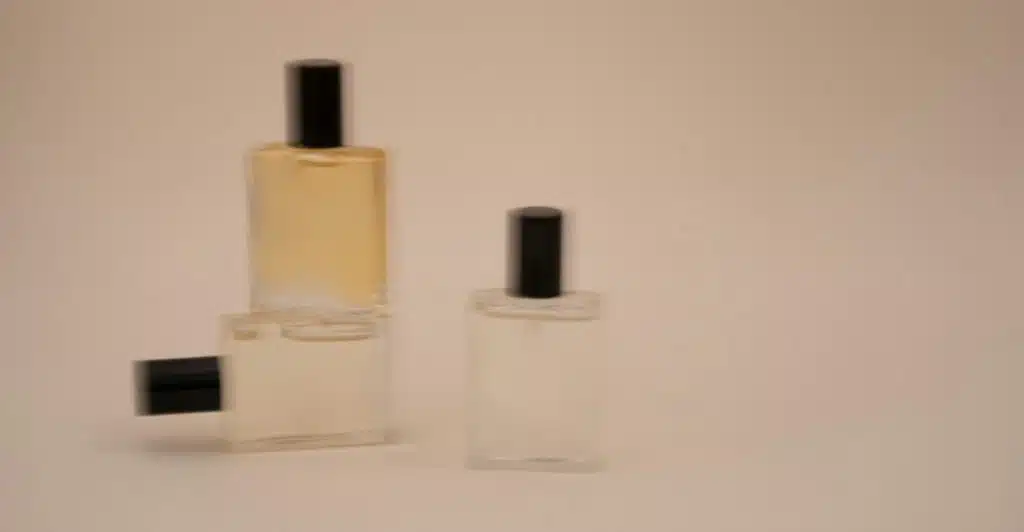 Three blurred perfume bottles with black caps sitting on a light-colored surface.
