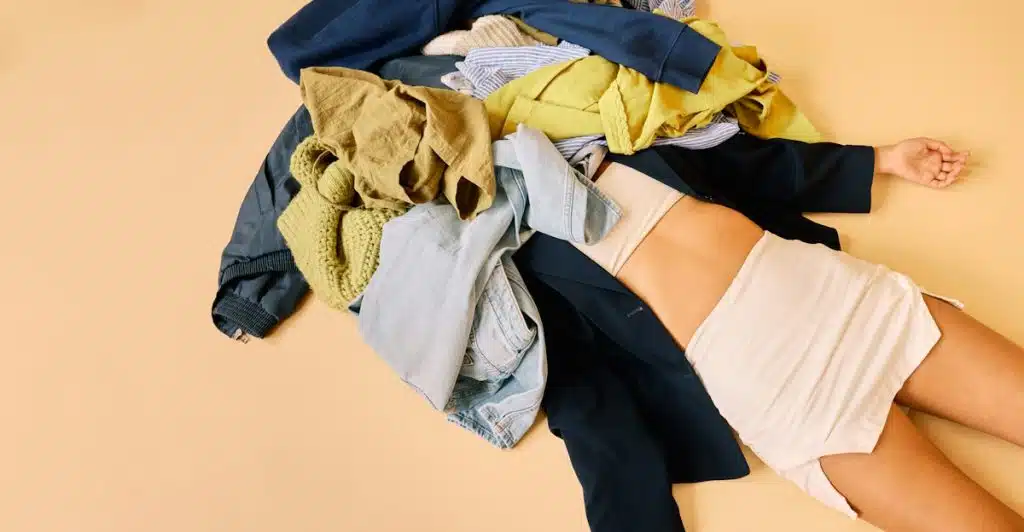 A person lying under a pile of assorted clothing.