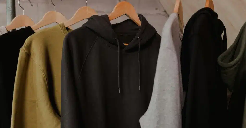 Clothes in neutral colors hanging on wooden hangers in a closet.