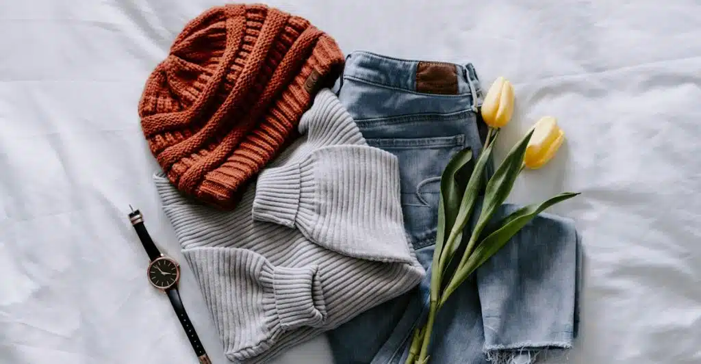 Folded clothing items and accessories arranged on a white bed with tulips.