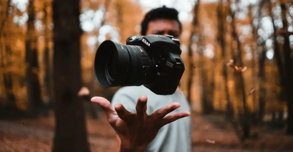 A person holding a DSLR camera in their hands in a forest setting.