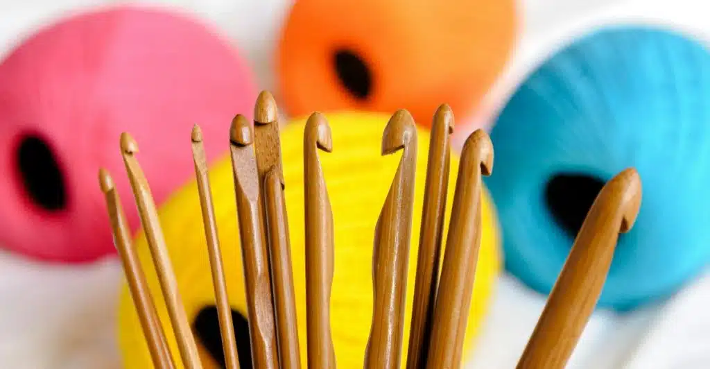 A close-up of several crochet hooks with colorful yarn in the background.