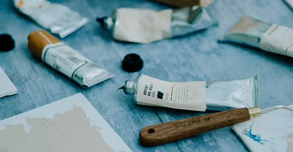 Painting supplies, including tubes of paint and a palette knife, arranged on a table.