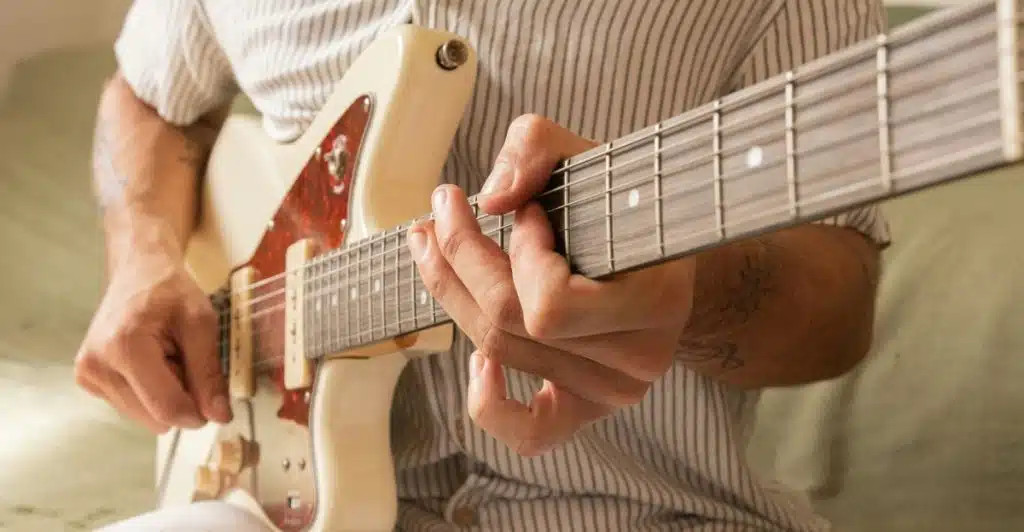 Close-up of a person's hands playing chords on an electric guitar.