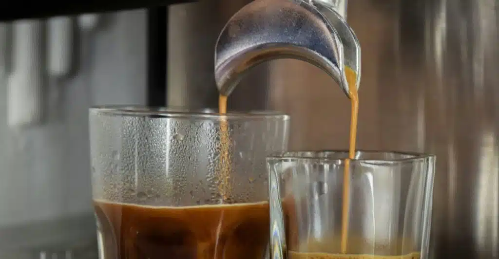Close-up of coffee being poured from a coffee machine into two glasses.