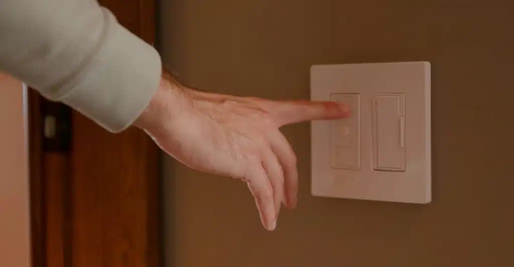 A hand adjusting a dimmer light switch on a wall.