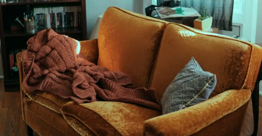 A cozy living room corner with a golden-yellow couch and a throw blanket.