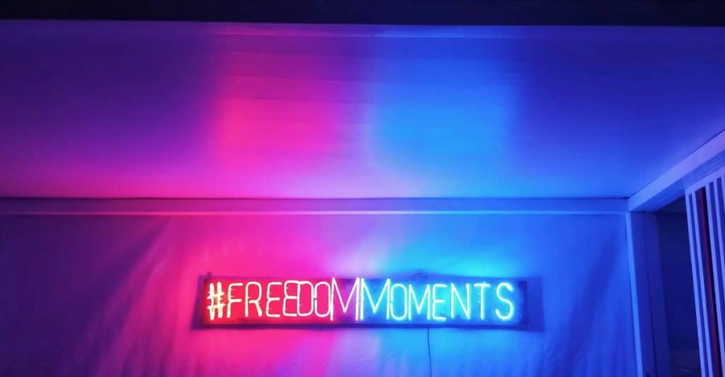 A neon sign that says "#FREEDOMMOMENTS" with a purple and blue glow.