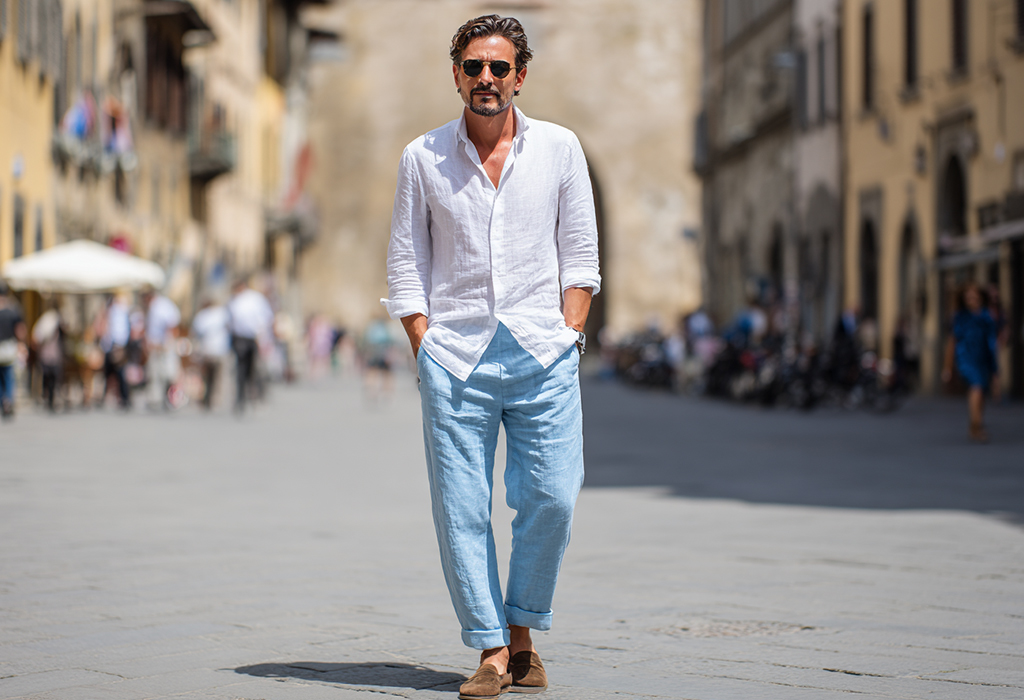 man wearing relaxed, pale blue chambray pants with a flowy white linen shirt in a sunny climate