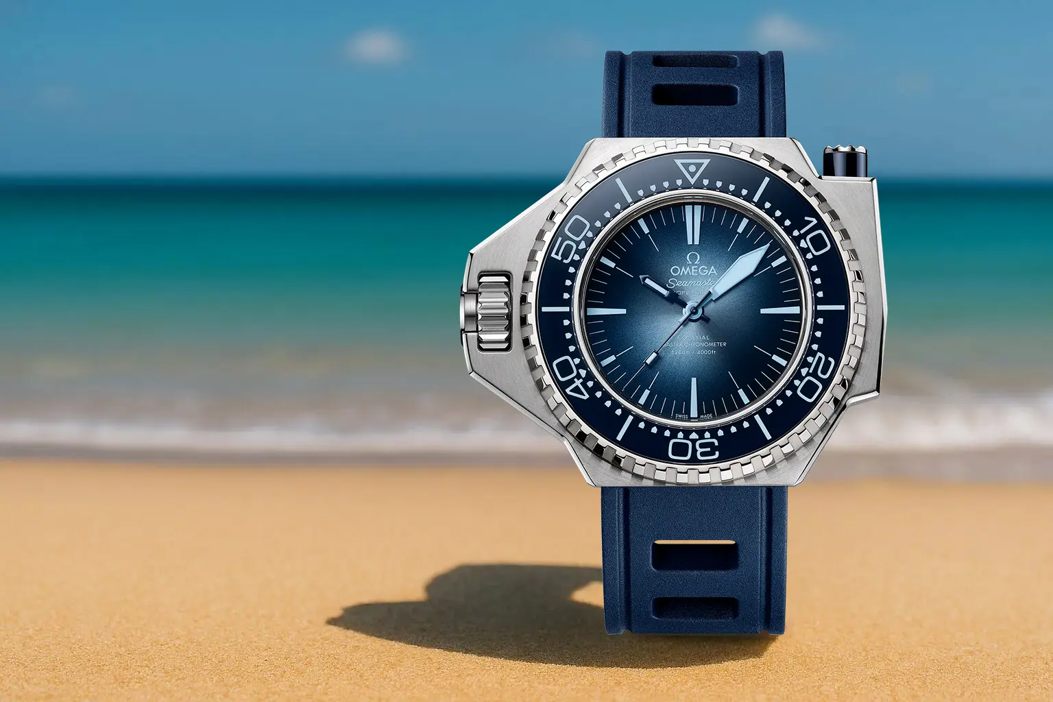 Omega Seamaster Ploprof dive watch with a bold case design and blue gradient dial, standing on golden sand with turquoise ocean in the background