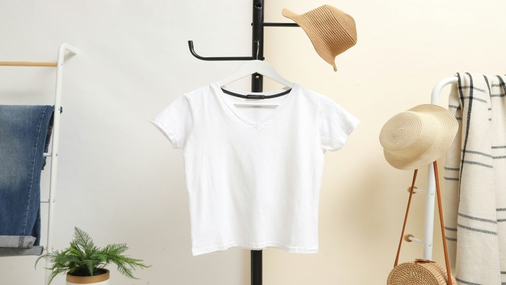 A white V-neck shirt hangs on a coat rack.