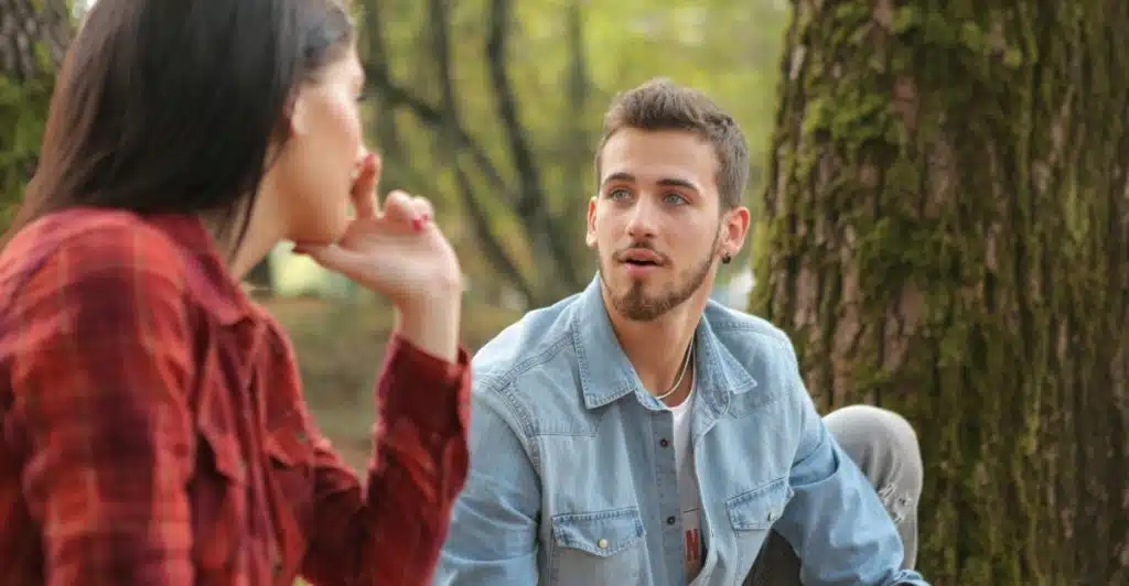 A man listening intently to a woman speaking in a wooded area.